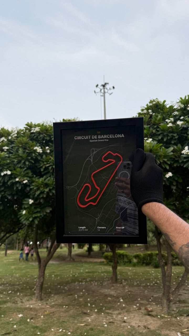Hand holding a artwork of Circuit de Barcelona with black background and red track with trees and people in the background