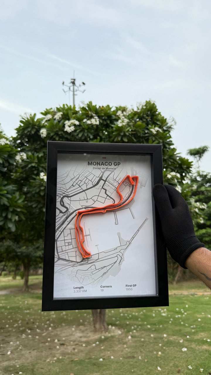 Person holding a framed artwork of Monaco GP with white background and orange track with trees and grass in the background