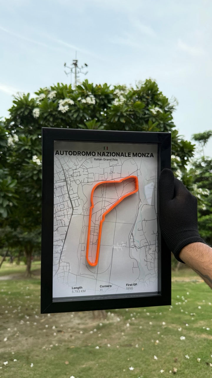 Person holding a framed artwork of Autofromo Nationale Monza with white background and orange track with trees and grass in the background
