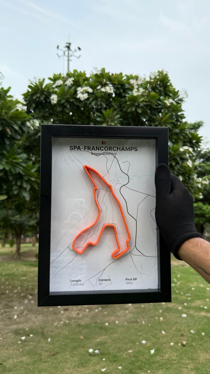 Person holding a framed artwork of Spa-Francorchamps with white background and orange track with trees and grass in the background